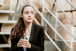 Jeune femme pensive assise dans sur une marche d'escalier tenant un café