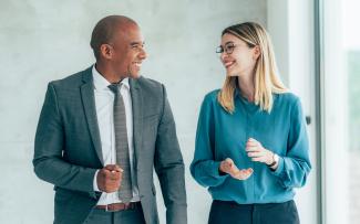 Deux collègues souriants marchant dans un corridor de bureau et discutant